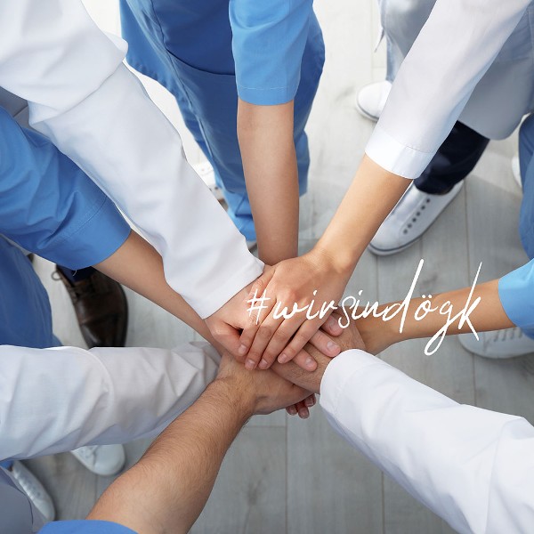 Mehrere Personen stehen im Kreis und legen die H&auml;nde &uuml;bereinander. Dar&uuml;ber der Schriftzug #wirsind&ouml;gk / Credit: Andrey Popov/shutterstock.com